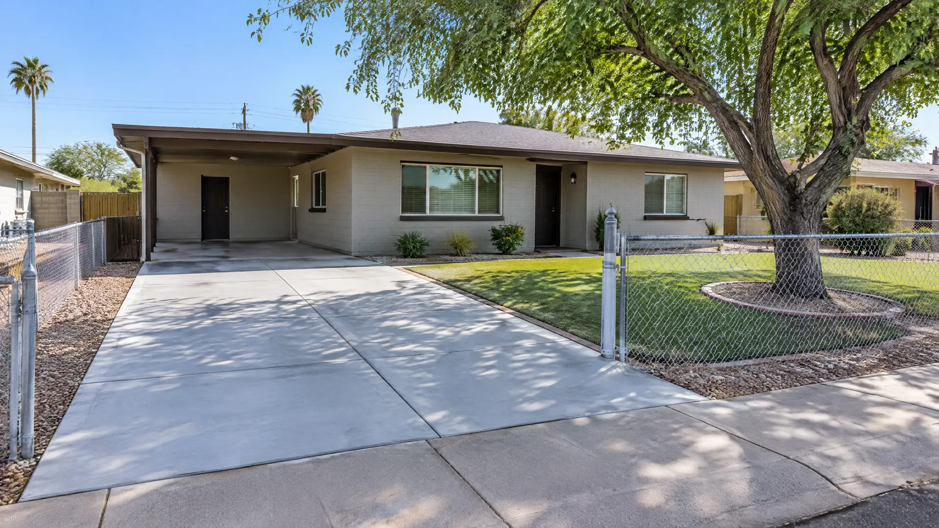 Freshly replaced concrete driveway at a modest 1960s ranch-style block home in west Phoenix with a chain-link fence, a shade tree and a clean front yard