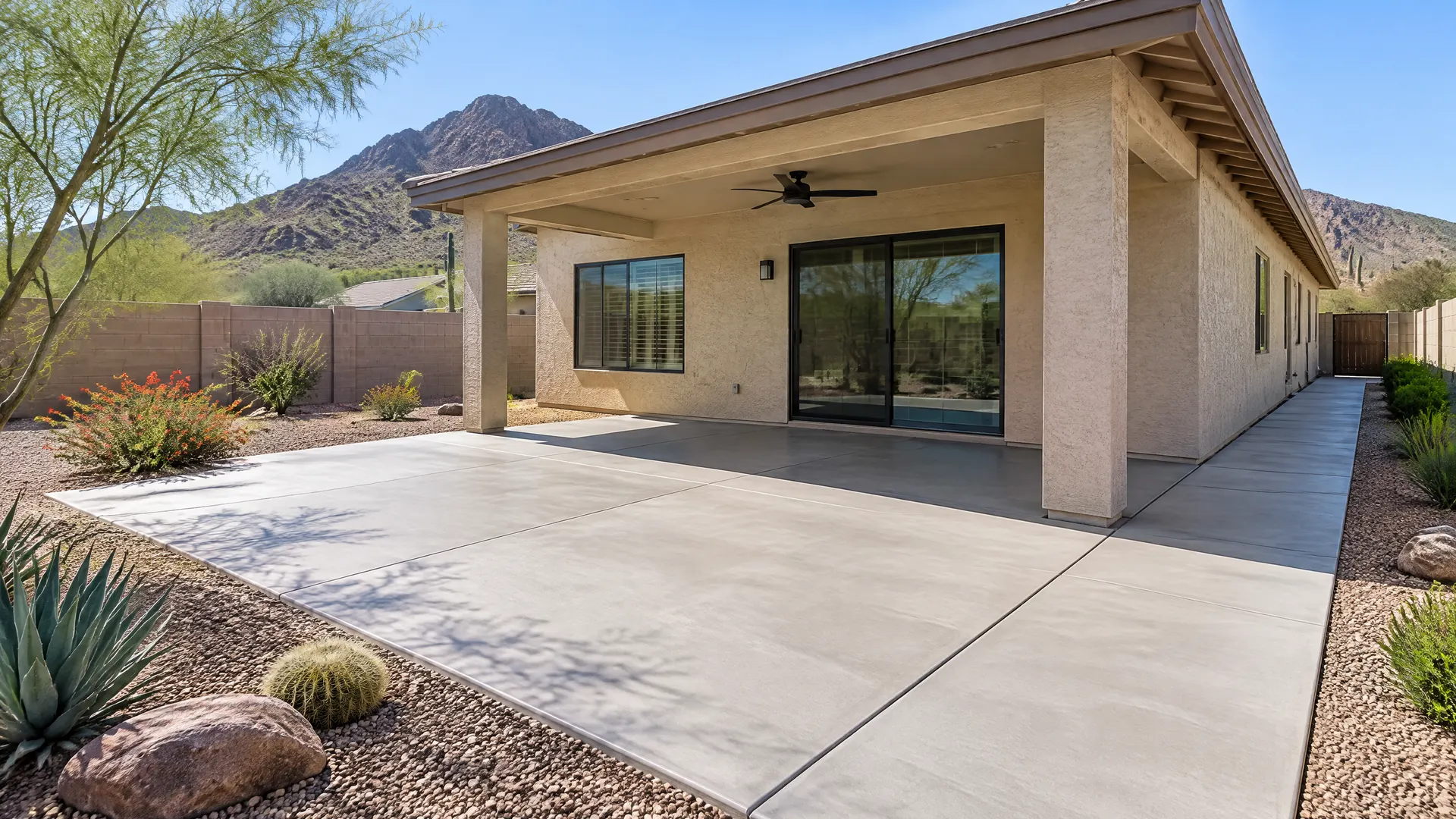 New concrete patio and side walkway at a 1970s single-story stucco home in north Phoenix near Piestewa Peak, desert landscaping and a block wall, clear sky